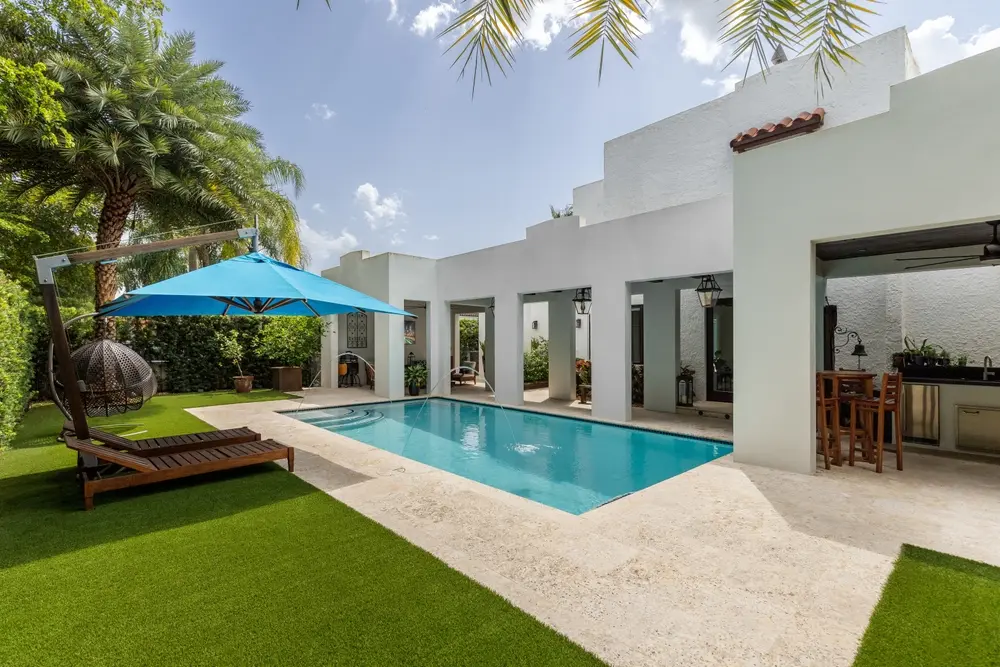 Backyard with swimming pool, artificial grass, stone path, chairs and an umbrella