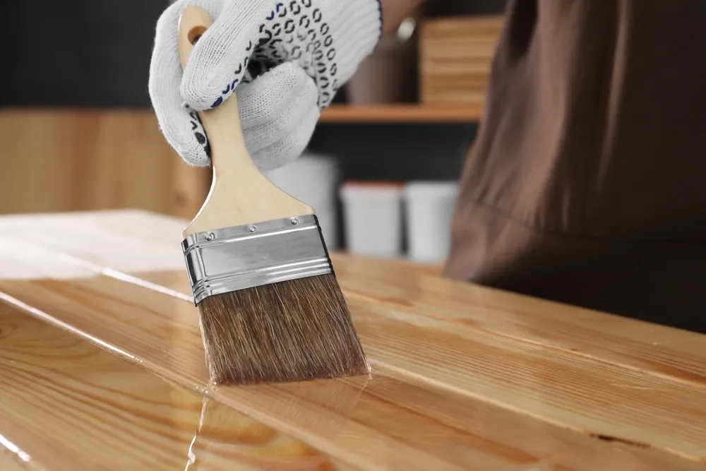 person applying varnish with a brush to a wooden surface